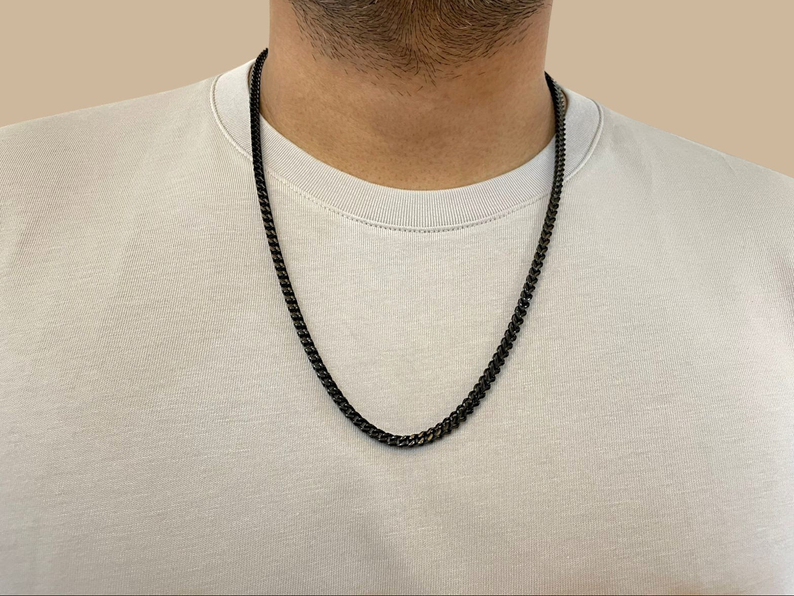 Person wearing a black chain necklace against a beige background
