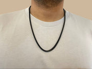 Person wearing a black chain necklace against a beige background